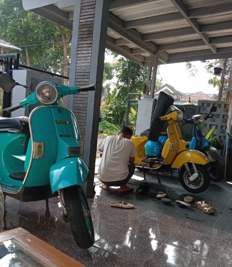 Tiga Vespa klasik berwarna tosca, kuning, dan biru di garasi rumah, sementara salah satunya sedang dikerjakan
